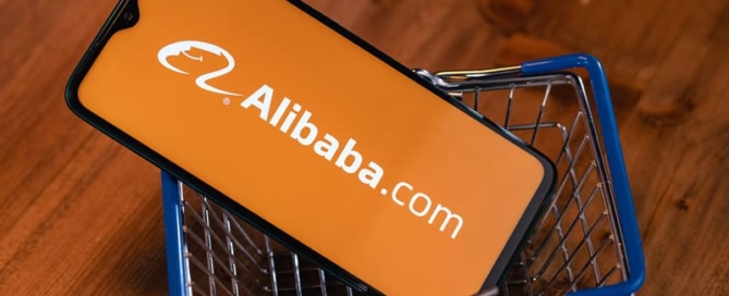 A mobile phone in a mini shopping cart showing the Alibaba.com logo