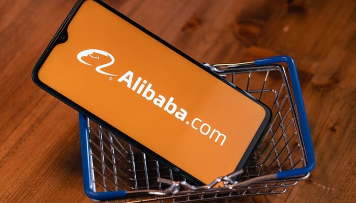 A mobile phone in a mini shopping cart showing the Alibaba.com logo